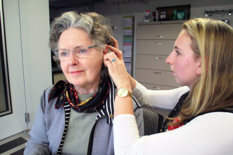 Audiology graduate student clinician fits an adult patient with a hearing aid.