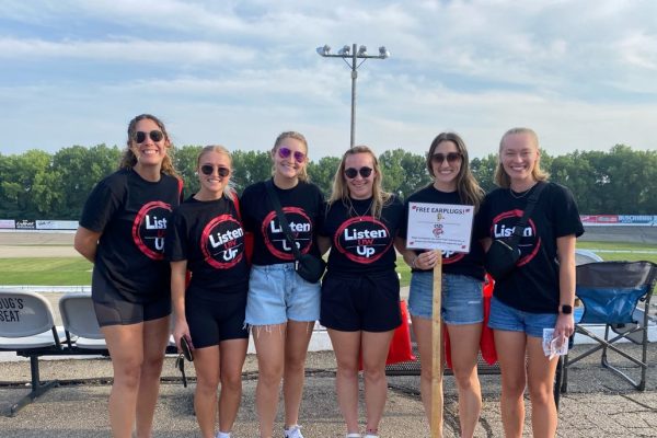 Graduate student clinicians at a loud outdoor motorsport event, where they give out earplugs and talk about the importance of safe listening practices.
